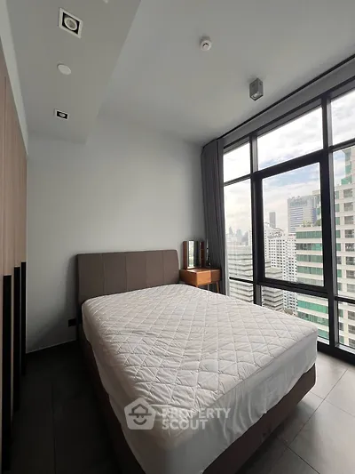 Modern bedroom with large windows offering stunning city views in a high-rise apartment.