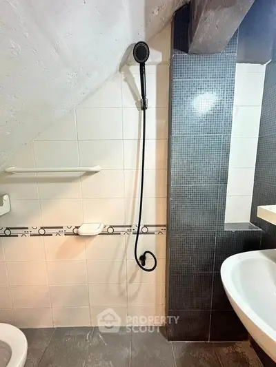 Compact bathroom with modern showerhead and sleek tile design under sloped ceiling.