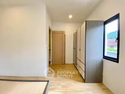Spacious bedroom with wooden flooring and large window offering natural light.