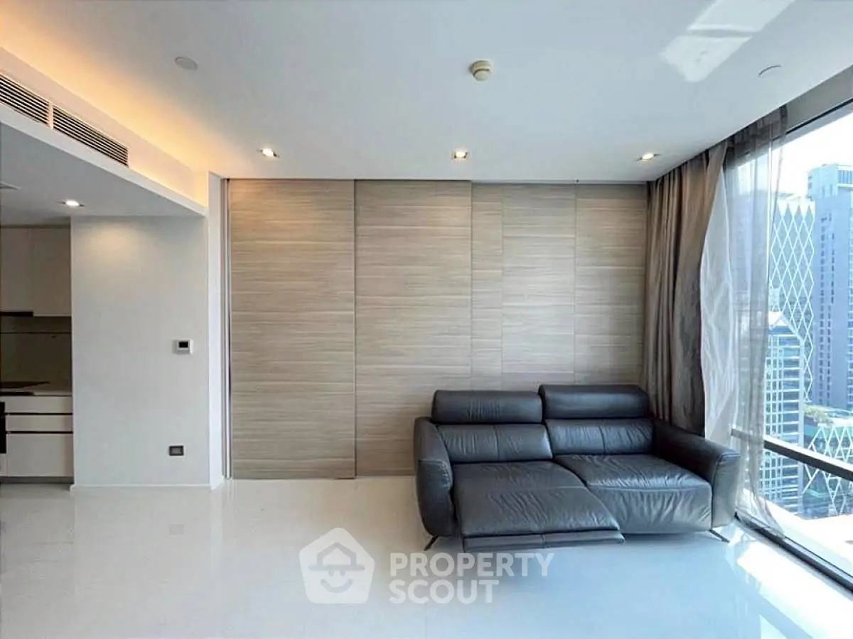 Modern living room with sleek black sofa and city view through large windows.
