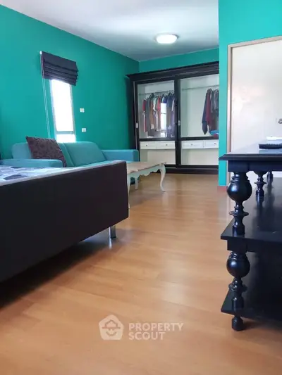 Spacious living room with modern decor and large wardrobe, featuring teal walls and wooden flooring.