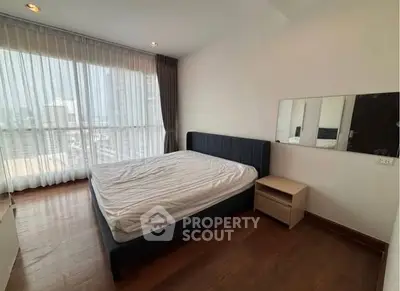 Spacious bedroom with large window offering city views, featuring a modern bed and wooden flooring.