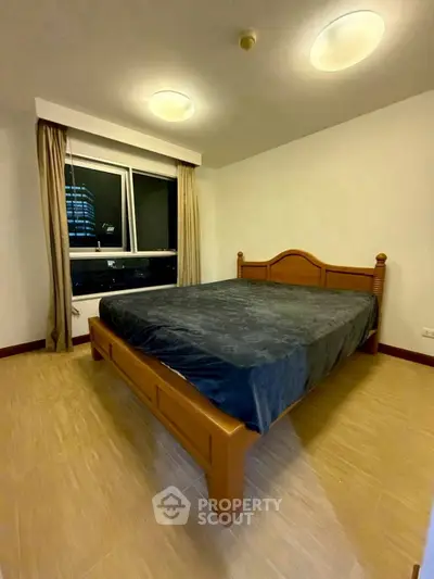 Spacious bedroom with large window and elegant wooden bed frame in modern apartment.
