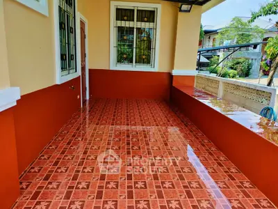 Charming tiled balcony with vibrant red accents and lush garden view.