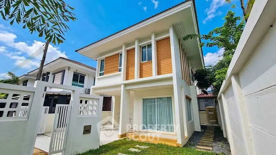 Modern two-story house with large windows and a spacious yard under a clear blue sky.