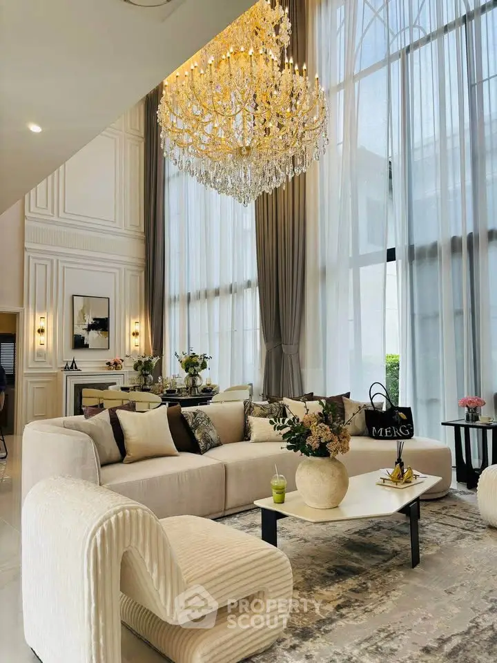 Luxurious living room with high ceilings, elegant chandelier, and plush furniture in a modern home.