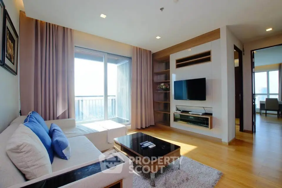 Modern living room with cozy sofa, wall-mounted TV, and large window offering natural light.