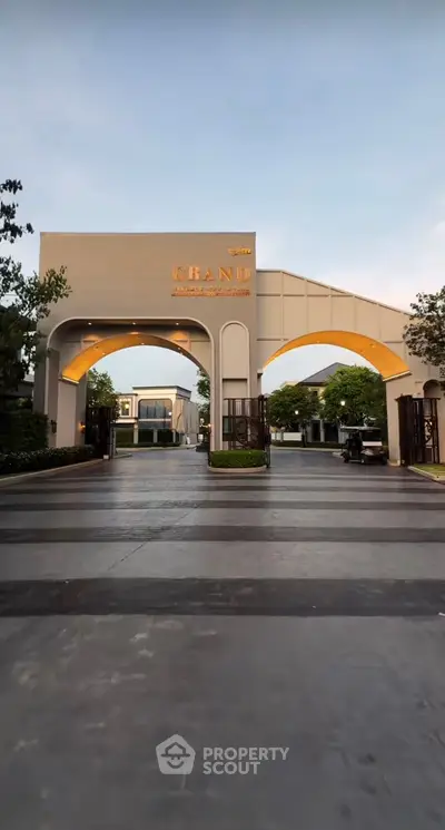 Elegant entrance of a modern residential complex with grand archway and lush surroundings.