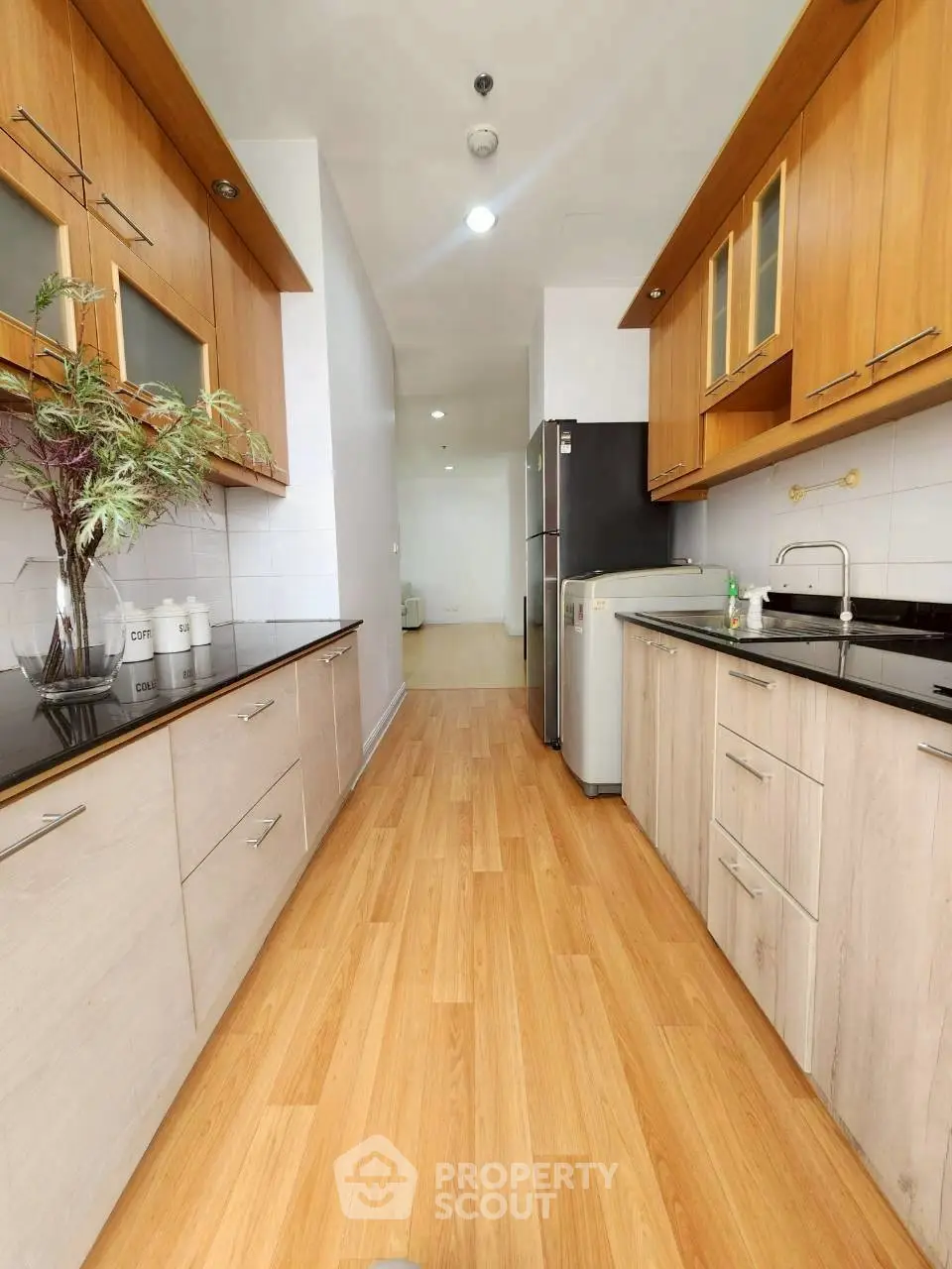 Modern kitchen with wooden cabinets and sleek appliances in a bright, narrow layout.