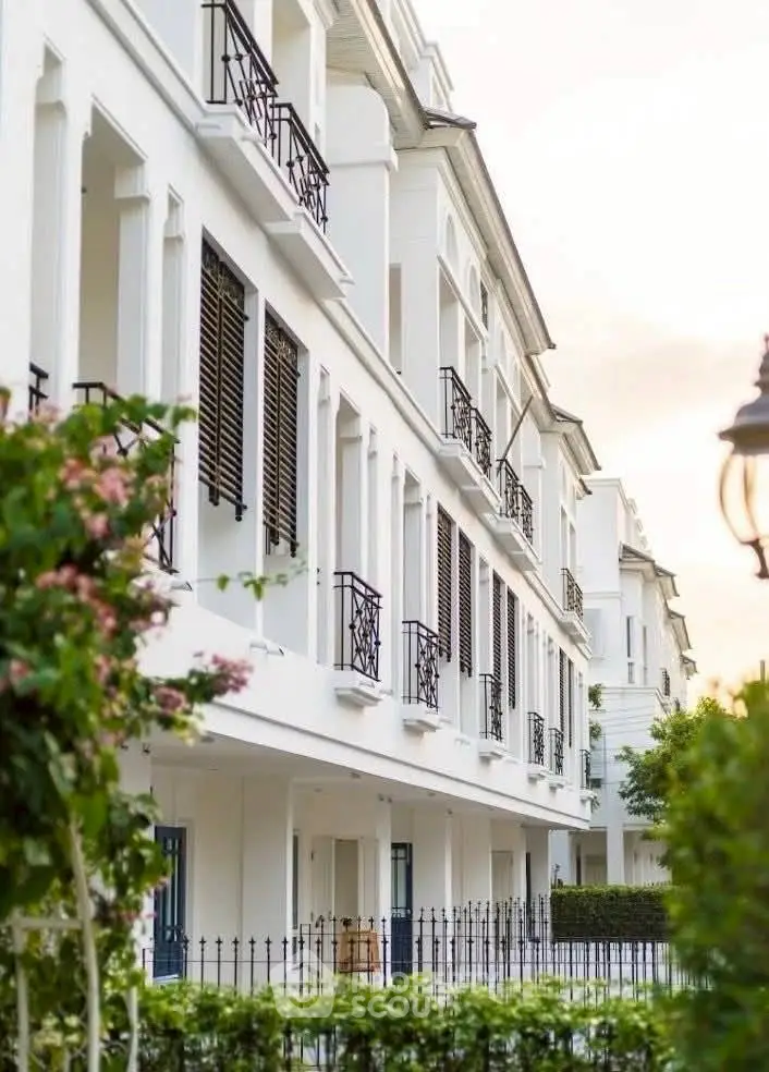 Elegant white residential building with black railings and lush greenery