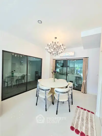 Elegant dining area with modern chandelier and glass doors opening to a serene view.