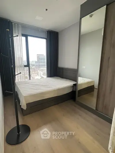 Modern bedroom with large window and mirrored wardrobe offering city views.