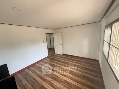 Spacious empty room with wooden flooring and large window, perfect for customization.