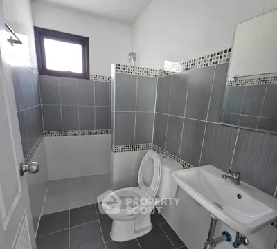 Modern bathroom with sleek gray tiles and white fixtures, featuring a toilet and sink under natural light.