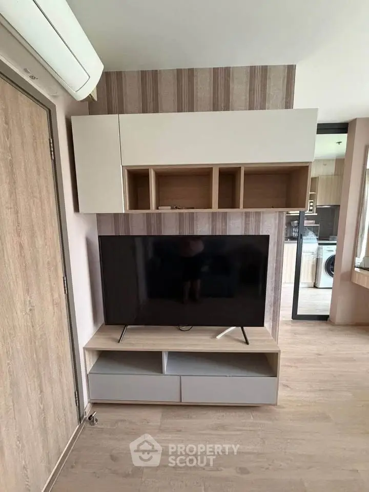 Modern living room with stylish TV unit and open kitchen layout, featuring sleek wood finishes and ample storage.
