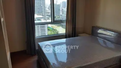 Modern bedroom with city view, featuring a large window and sleek furnishings.