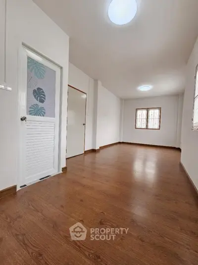 Spacious and well-lit empty room with polished hardwood floors, white walls, and multiple windows creating a warm, inviting atmosphere.