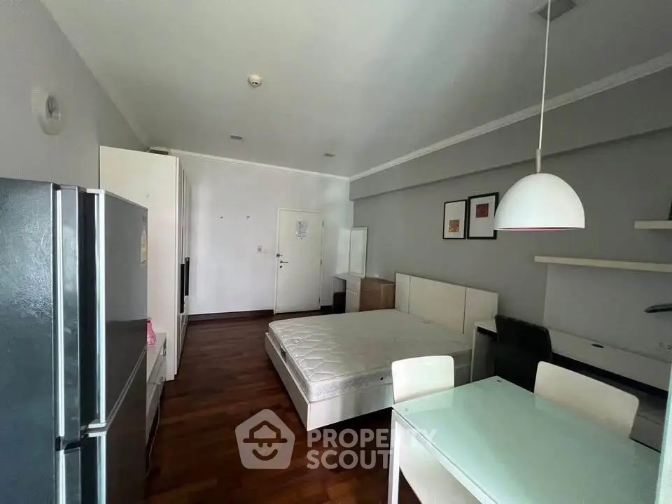 Modern studio apartment with open layout, featuring a cozy bed, dining area, and sleek kitchen appliances.