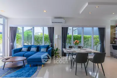 Spacious modern living room with blue sofa and dining area, large windows, and garden view.
