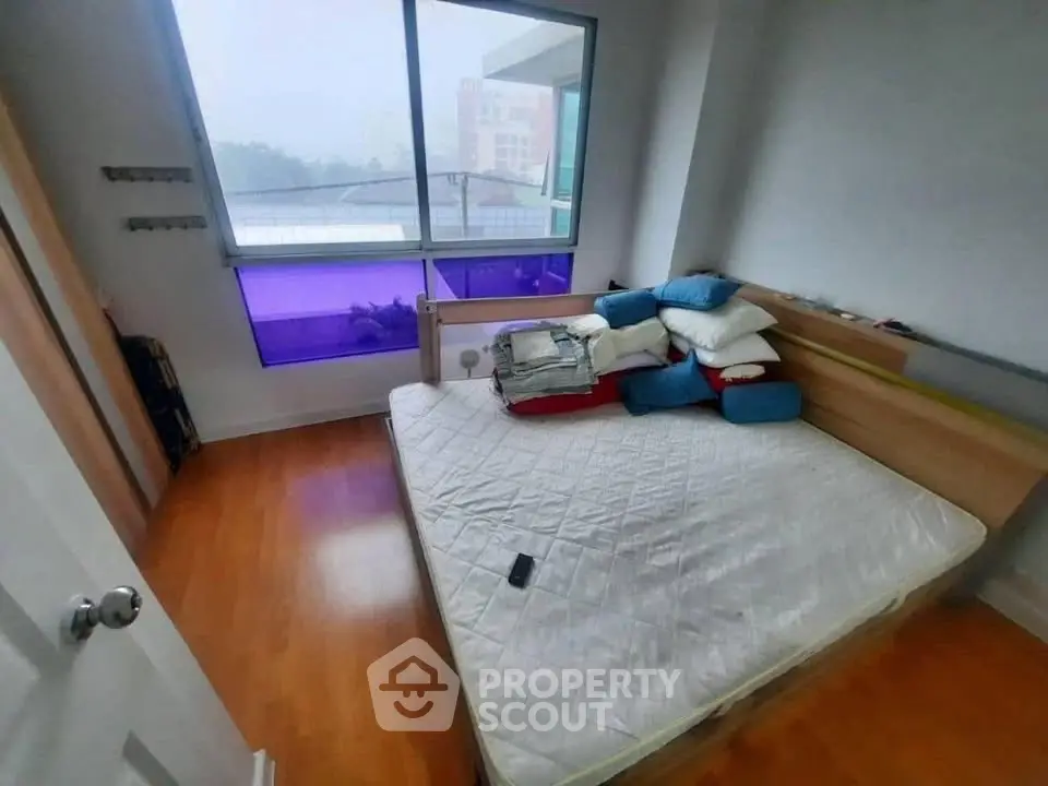 Cozy bedroom with large window and wooden flooring, perfect for relaxation.