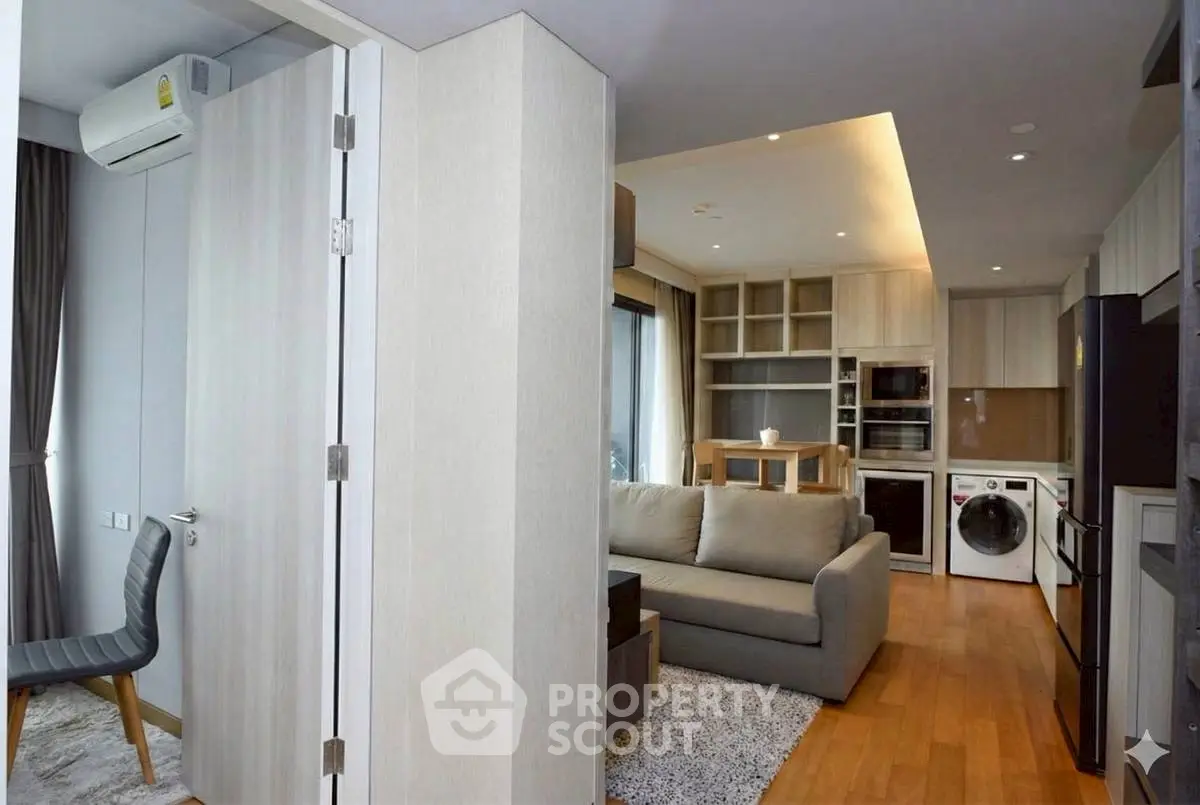 Modern open-plan living room with kitchen and laundry appliances, featuring sleek design and wooden flooring.