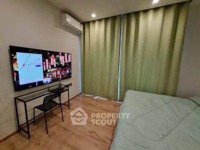 Modern bedroom with wall-mounted TV and air conditioning, featuring elegant green curtains and wooden flooring.