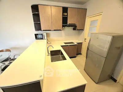 Modern kitchen with sleek cabinets, fridge, and microwave in a stylish apartment.