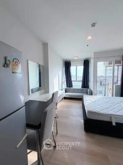 Modern studio apartment with natural light and city view, featuring a cozy bed and dining area.