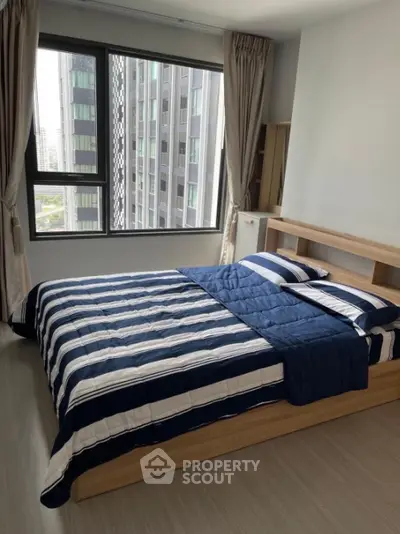 Modern bedroom with city view and stylish striped bedding in high-rise apartment.