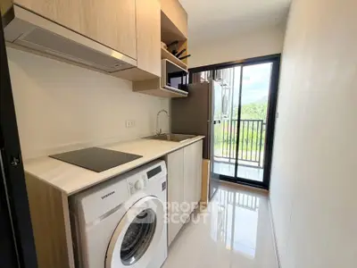 Modern kitchen with washing machine and sleek appliances, featuring a bright view through large glass doors.
