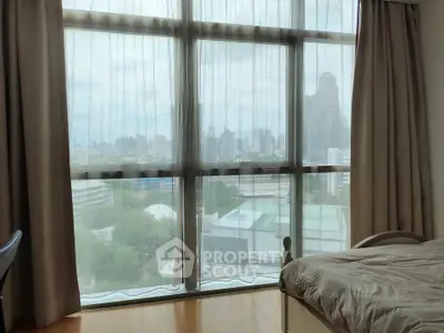 Spacious bedroom with large window offering stunning city skyline view, perfect for urban living.