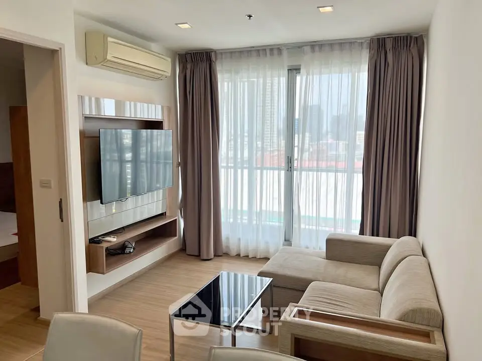 Modern living room with large windows and city view, featuring a cozy sofa and wall-mounted TV.