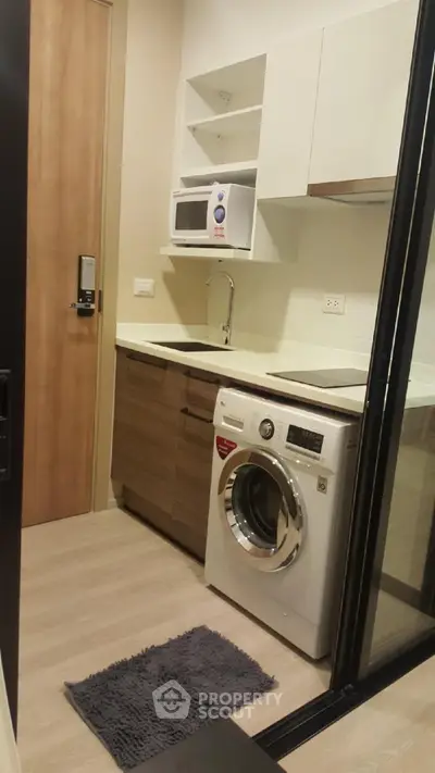 Modern compact kitchen with washing machine and microwave in a stylish apartment.