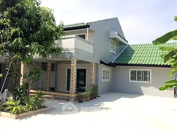 Charming two-story house with green roof and spacious driveway, surrounded by lush greenery.