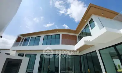 Modern luxury home exterior with large glass windows and sleek architectural design under a clear blue sky.