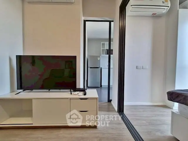 Modern living room with sleek TV setup and view into a contemporary kitchen.