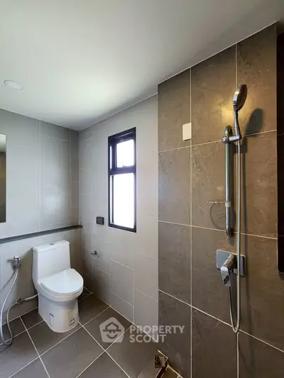 Modern bathroom with sleek tiles and shower, featuring a large window for natural light.