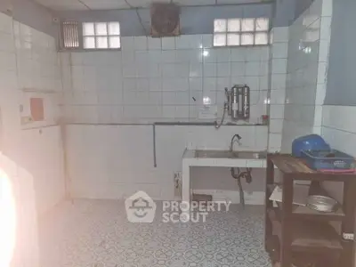 Spacious kitchen with tiled walls and floor, featuring a sink and storage shelves.