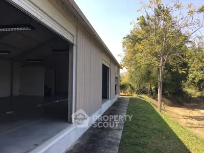 Spacious industrial warehouse with open garage doors and lush greenery surroundings.