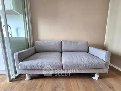 Modern living room with stylish gray sofa and wooden flooring, adjacent to a sleek kitchen area.