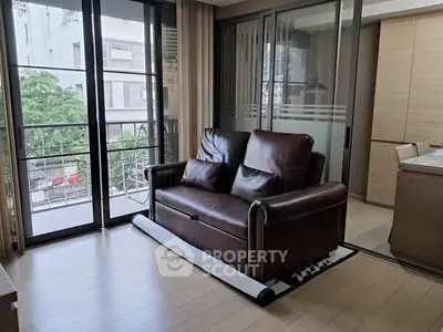 Modern living room with leather sofa and large windows overlooking a lush green view.