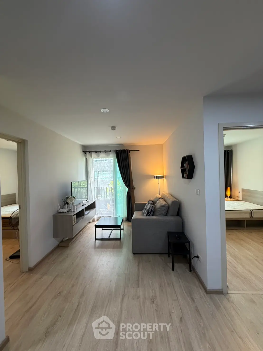 Modern living room with cozy sofa and natural light, adjacent to bedrooms, featuring sleek wooden flooring.