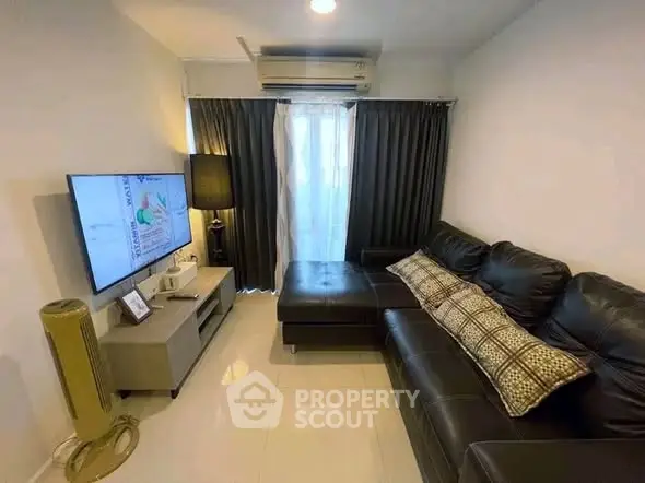 Cozy living room with modern black leather sofa and flat-screen TV, perfect for relaxation.