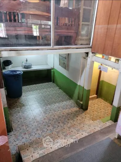 Unique split-level interior with tiled flooring and green accents, featuring a sink and ample space for storage or utility use.
