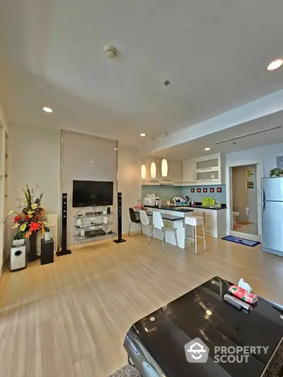 Modern open-layout living room with kitchen, featuring sleek decor and ample natural light.