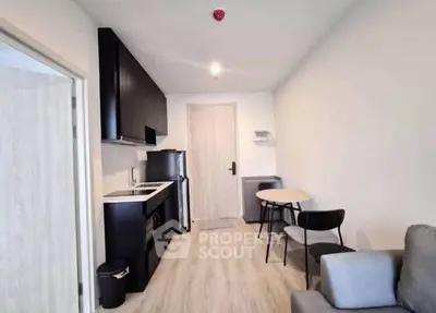 Modern compact kitchen and dining area in a cozy apartment with sleek black cabinets and light wood flooring.