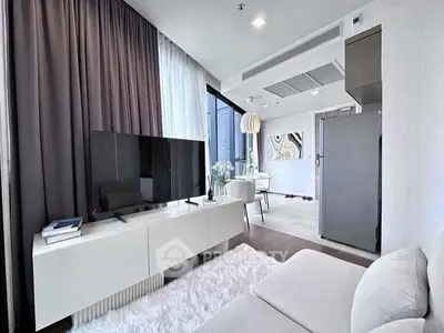Modern living room with sleek furniture and large TV, open to dining area with stylish decor.