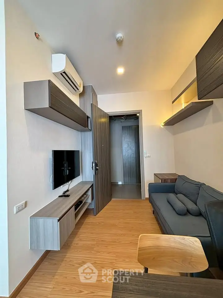 Modern living room with sleek furniture and wooden flooring, featuring a wall-mounted TV and air conditioning.