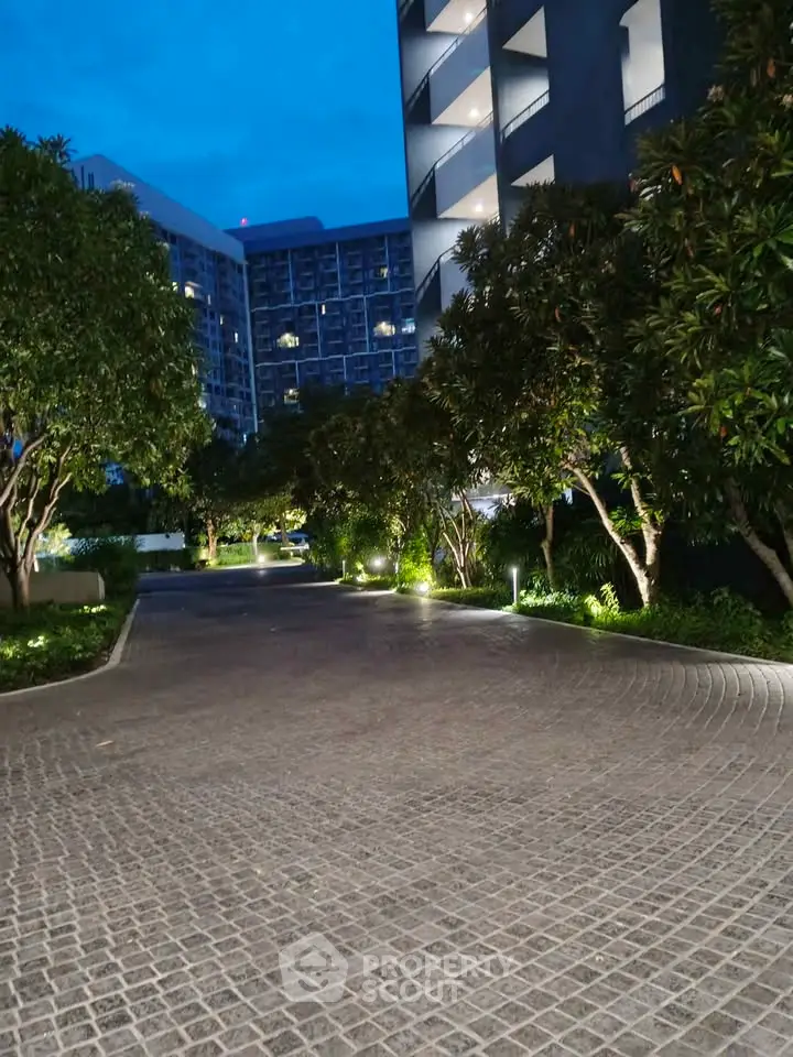 Elegant evening view of modern residential building entrance with lush greenery and ambient lighting.