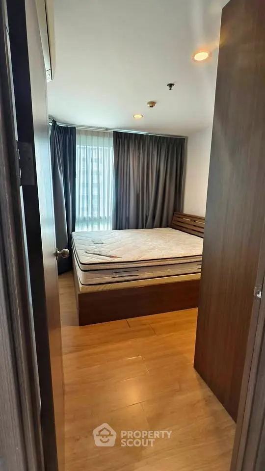 Cozy bedroom with wooden flooring and large window, featuring a comfortable bed and stylish curtains.